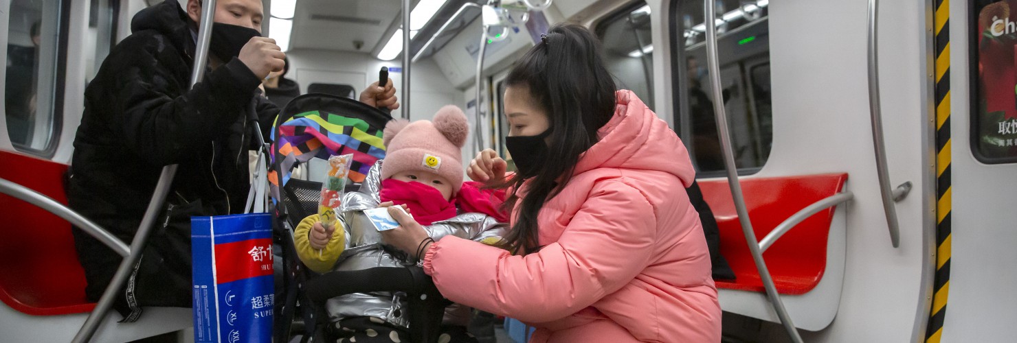 People wearing face masks attend to a child in a stroller as they ride a subway train in Beijing