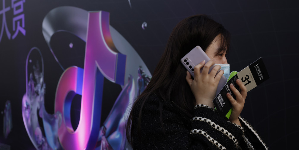 A woman speaks on her phone near the logo for Douyin in Beijing 