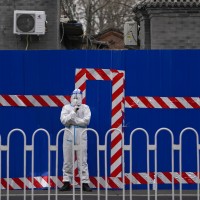A security guard wearing a protective suit stand watch over a barricaded community that was locked down for health monitoring following the COVID-19 case detected in the area, Tuesday, March 22, 2021, in Beijing