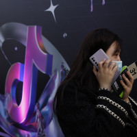A woman speaks on her phone near the logo for Douyin in Beijing 